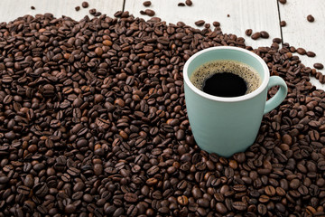 Fresh cup of coffee surrounded by freshly roasted Arabica beans on wooden background.