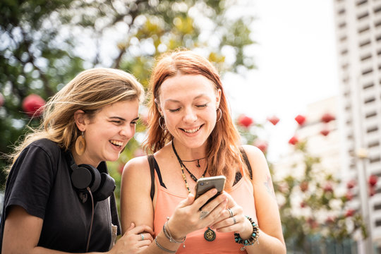 Two young women looking at the mobile phone while laughing in the street
