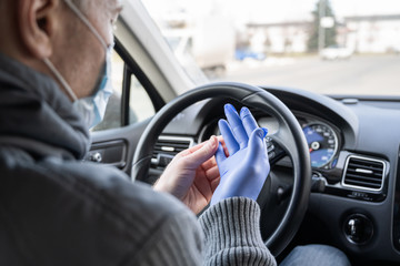 Man in the medical mask puts on rubber gloves for protect himself from bacteria and virus while driving a car. Coronavirus. Pandemic