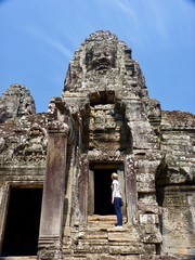 Ruins of Angkor, face tower of Bayon temple with blond woman looking up, Angkor Wat, Cambodia