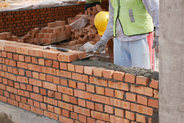 Brickwork by construction workers at the construction site. Workers laying the clay brick and stacked it together using mortar to form the wall. 