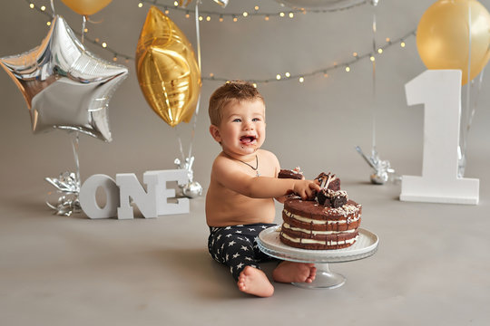 Smash cake party. Little cheerful birthday boy with first cake. Happy infant baby celebrating his first birthday. Decoration and photo zone for first year. One year baby celebration. Grey decor.