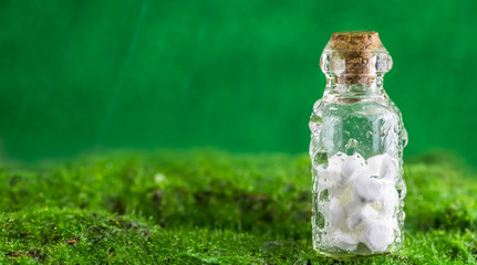 White tablets in a bottle of water droplets on green background