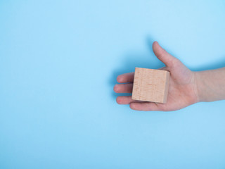 close-up of a hand placing wooden block on a blue background. A child's hand holds a cube. Space for your text