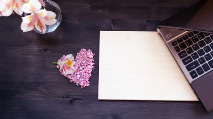 Flat lay home office desk. Working at home women workspace with laptop, flowers bouquet on a dark brown wooden background.