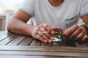 a man is holding a glass with a drink and a cigarette. pernicious habits. hazardous to health.