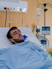 Teenage boy with a beard and wearing an oxygen mask, in a hospital room