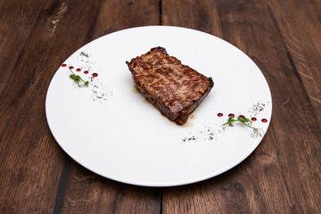 Juicy Striploin Steak: thin edge of the beef, thyme and olive oil in a plate on a wooden table.