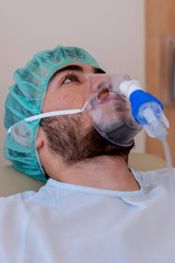 Teenage boy with a beard and wearing an oxygen mask, in a hospital room