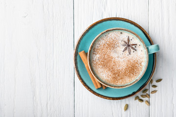 Masala tea in a ceramic cup with cardamom, star anise, cinnamon and ginger on a wooden background. Antiviral drink for immunity. Top view, place for text.