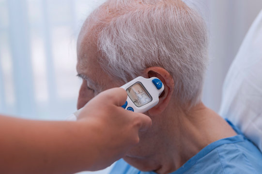 Close-up of a nurse taking an elderly man's temperature with a digital thermometer in her ear