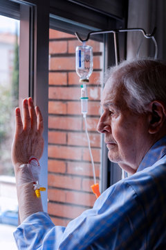 90-year-old man with a catheter in his arm, looking out a hospital window