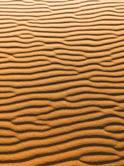 Orange vertical texture of sand dune. Abstract shape, background, shadow and sun light. Sahara desert.