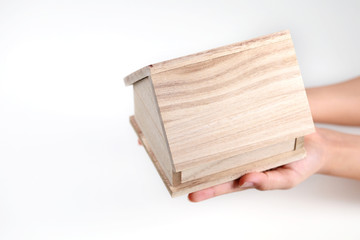 Close-up of hand holding a wooden figure of house against light background