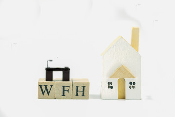 Text of WFH mean work from home with miniature table and wood home.