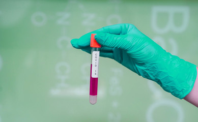 A rubber-gloved hand holds one test tube with coronavirus