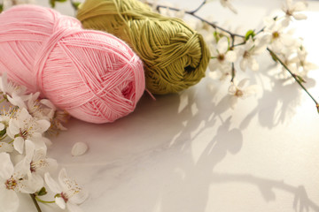 Colorful yarn balls with spring flowers on light background.