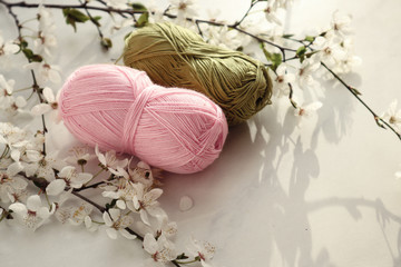 Colorful yarn balls with spring flowers on light background.