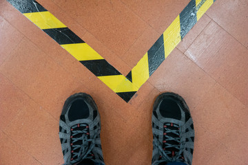 Pair of male boots standing behind security safety roll tape on the floor top view