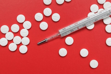 Thermometer and pills on red background.