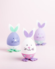 Funny kawaii cute bunny eggs in pastel colors on pink table top, Easter holiday concept. Easter decoration for kids still life, copy space