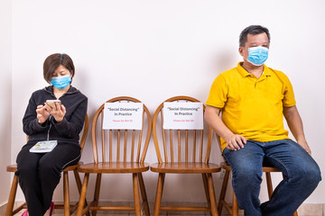 Obraz premium People with face mask seated in-between two chairs at public place with Social Distancing, Do Not Sit signage.