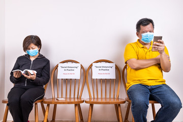 People with face mask seated in-between two chairs at public place with Social Distancing, Do Not Sit signage.