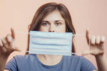 Portrait of young woman showing opened medical flu mask covering face on colored studio background, quarantine measures and life saving concept