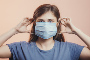 Portrait of young woman putting medical flu mask on face, on colored studio background, quarantine measures and life saving concept