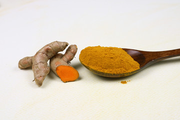 Turmeric powder in a wooden spoon and fresh turmeric roots isolated on a white background is an ingredient in turmeric foods and ingredients in skin care products. Turmeric helps the skin to be strong