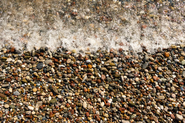 Colorful pebble beach and sea with waves. Wave rolls on the beach