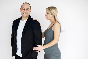 Young pretty blonde, expectant mother, stands next to her husband. Young couple, man and woman, beautifully and elegantly dressed, standing in studio on a white background. Pragnancy concept.