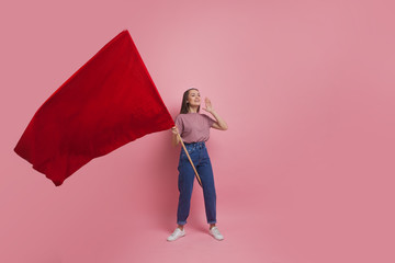 Young and beautiful girl with a red flag on a pink background. A socially active woman, to protest...