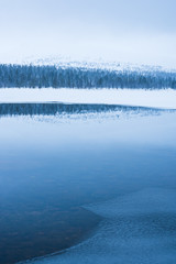 Reflections on still winter lake, Sweden.