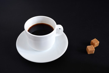 Set: a mug, saucer and two pieces of sugar. On black background.
