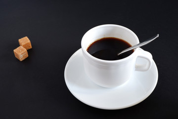 Set: a mug, a teaspoon, a saucer and two pieces of sugar. On black background.