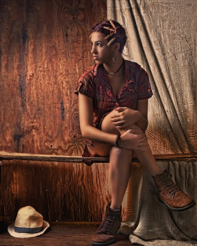 Joven campesina Santana con fondo de  madera con decoraci&oacute;n de pelillos de tender  y en pose tranquila y sexy con camisa a cuadros carmelita