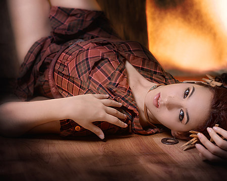 Joven campesina acostada sobre el piso de madera con decoración de pelillos de tender de madera y en pose tranquila y sexy con camisa a cuadros carmelita