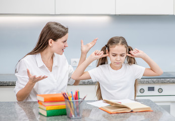 Sad girl covers her ears  while her mother scolds her for poor study. Family relationships