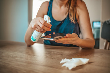 Woman holding a smartphone while removing dirt from the surface of the screen. Female wiping her mobile phone after usage in her room. My cellphone needs a good clean