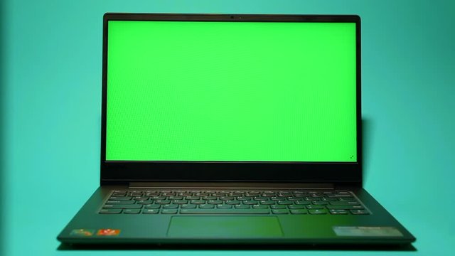 The laptop is on a blue background and shows a green screen display.  Laptop computer with green screen mockup on blue background.