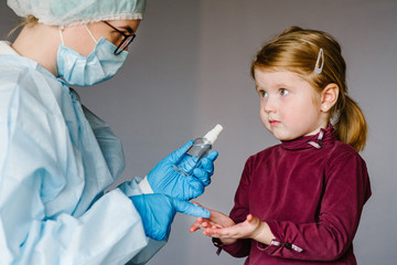 Coronavirus. Nurse or doctor in a protective suit, mask tells child how to use the sanitizer. Preventive measures against Covid-19 infection. Аntibacterial gel with alcohol-based hand-washing spray.