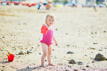 Adorable toddler girl playing with sand on the beach. Child spending vacation on the Atlantic coast in Normandy, France. Outdoor activities for kids