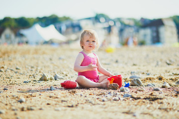 Adorable toddler girl playing with sand on the beach. Child spending vacation on the Atlantic coast in Normandy, France. Outdoor activities for kids