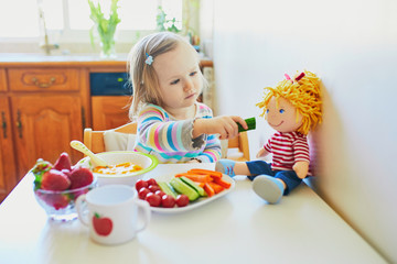 Adorable toddler girl eating fresh fruits and vegetables for lunch