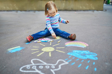 Fototapeta premium Adorable toddler girl drawing with colorful chalks on asphalt