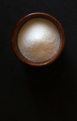 Zucchero bianco in una ciotola di legno, isolata su fondo scuro. Vista dall'alto.