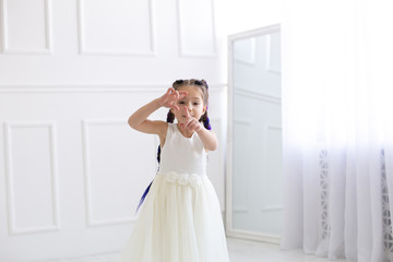 horizontal portrait of a five year old girl in a white dress who is having fun in a white studio