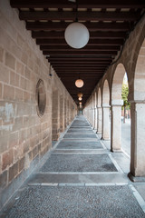 A Beautiful Perspective of an Aisle with Brick Walls on the left, Arches and Garden on the right and Stripes of Wooden Ceiling on top