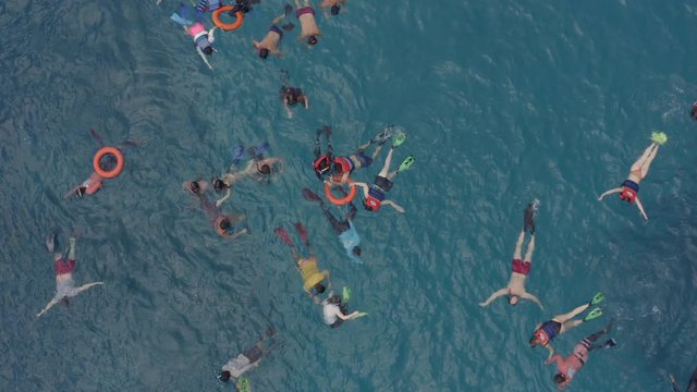 Group of snorkelers swimming in a blue water at the coral shoals observing underwater life with tourist boat adrift nearby, Nusa Penida, Bali, Indonesia. Rise up aerial shot.